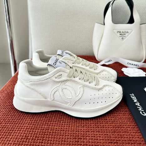 Elegant white sneakers featuring a sleek design with a logo and perforated detailing, showcased on a textured surface.